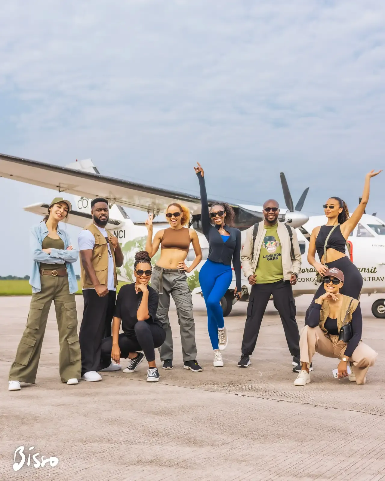 Le groupe des invités posant devant un petit avion à hélices sur le tarmac, en plein jour.